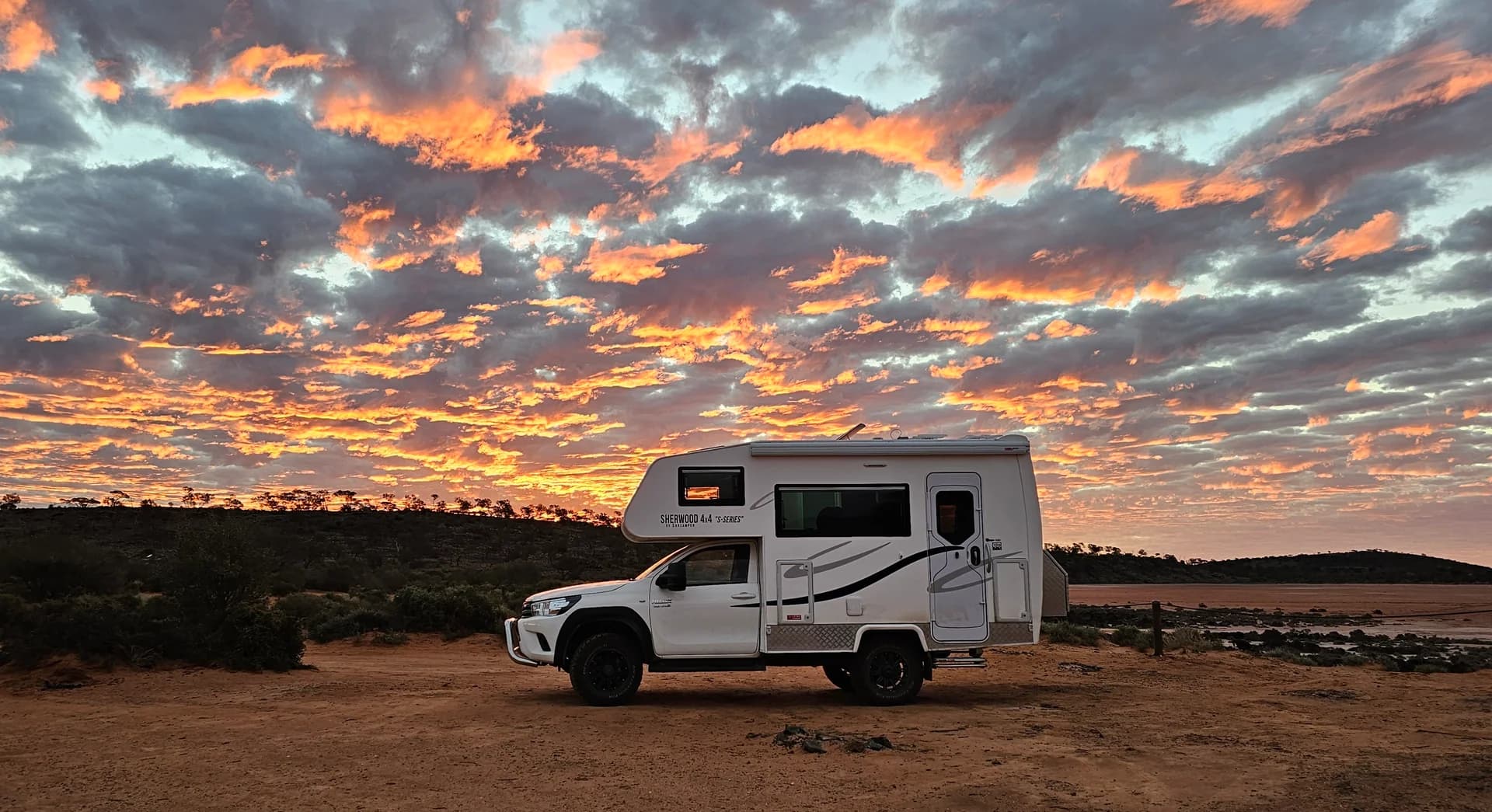 Suncamper silhouetted against a burning sunset on the salt pan of Lake Ballard, Western Australia